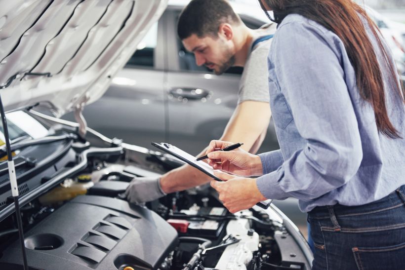A man mechanic and woman customer look at the car hood and discuss repairs.