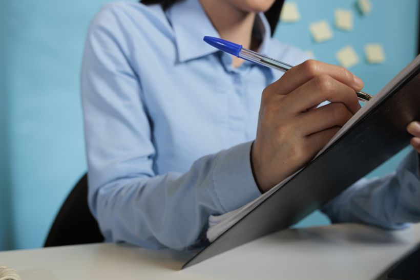 Female entrepreneur concentrating on writing in files and signing documents and papers about project on a clipboard.
