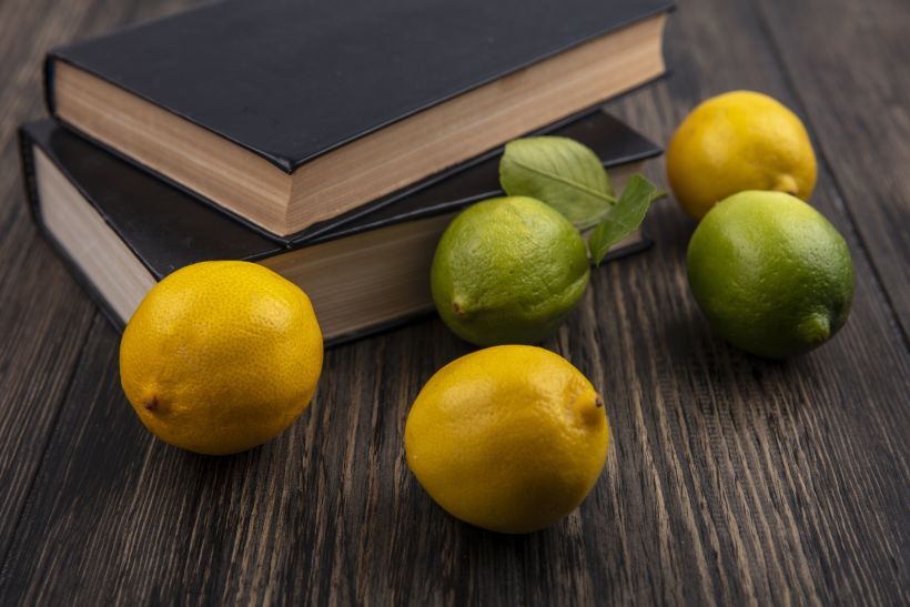 Front view lemons with limes and books on wooden background.