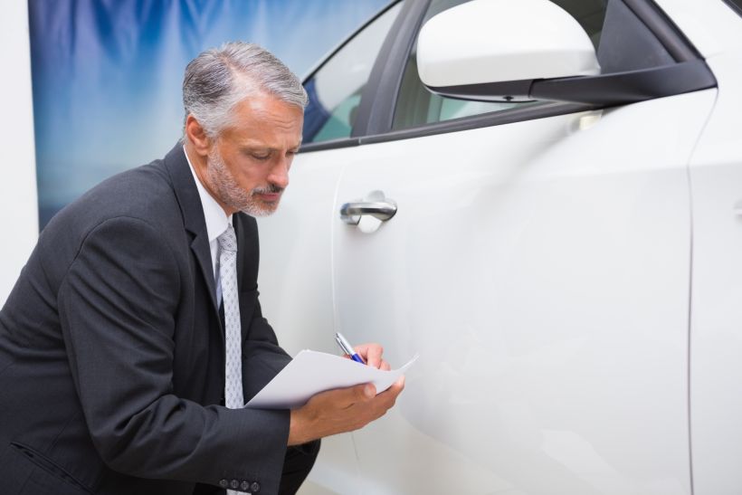 Businessman looking at car while writing on clipboard.