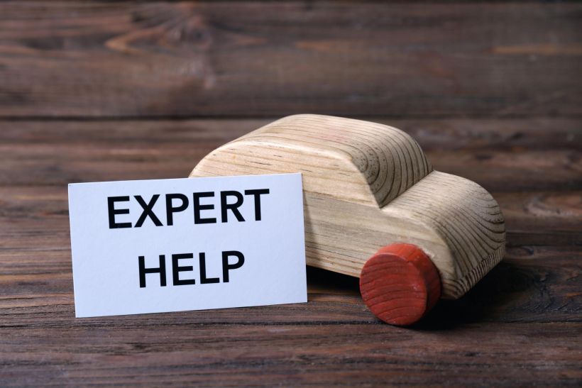 Wooden toy car and paper with phrase expert help on wooden background.