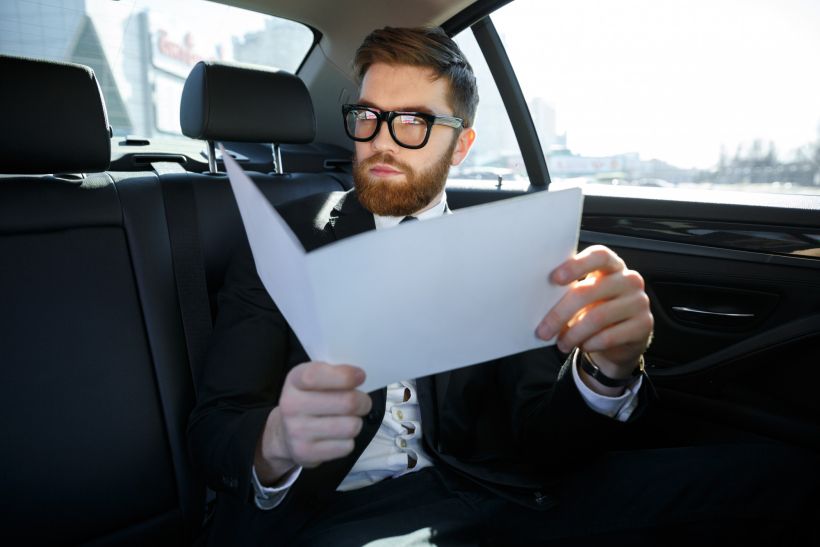 Businessman with documents driving on car back seat.
