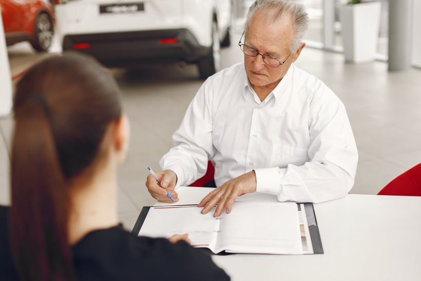 Old man sitting in a car salon and talking with manager.