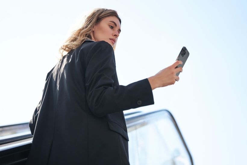 Successful businesswoman standing on escalator looking at mobile phone renewing her car registration.