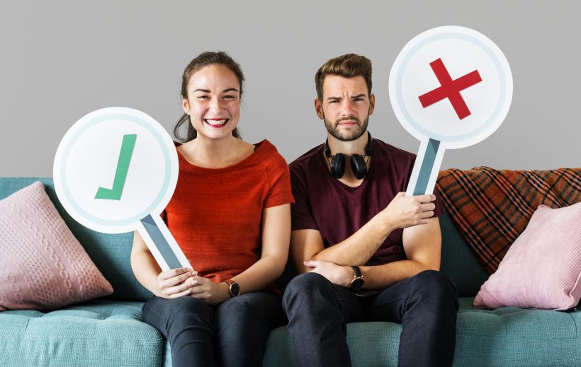 Cheerful couple holding vote icon sitting on a couch.
