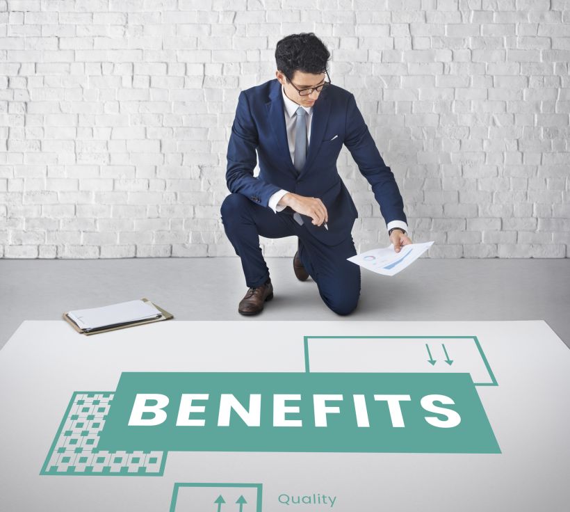 A young man stands next to a sign with the word “benefits” written on it.