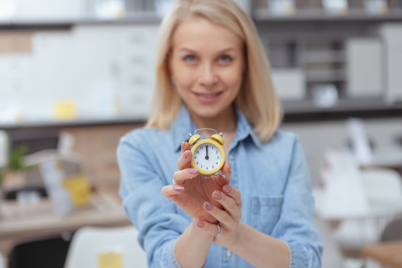 Small alarm clock in the hand of a beautiful happy woman.